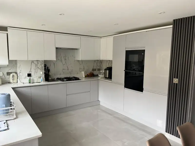 A fitted kitchen with grey base cabinets, white wall units and built-in ovens